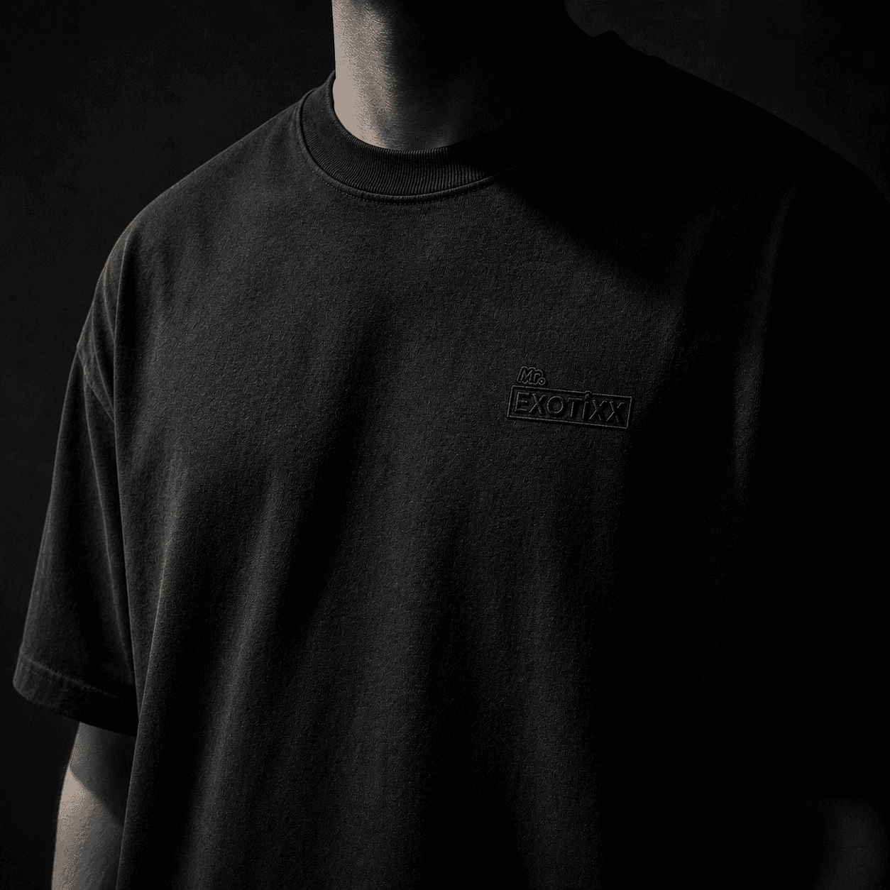 Front portrait of figure wearing the heavyweight black Mr. Exotixx tee, no face, tonal logo at left chest